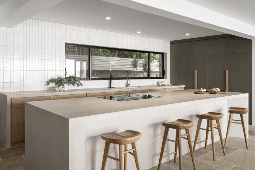 A dark, modern kitchen with artificial overhead lights that are above the kitchen bench